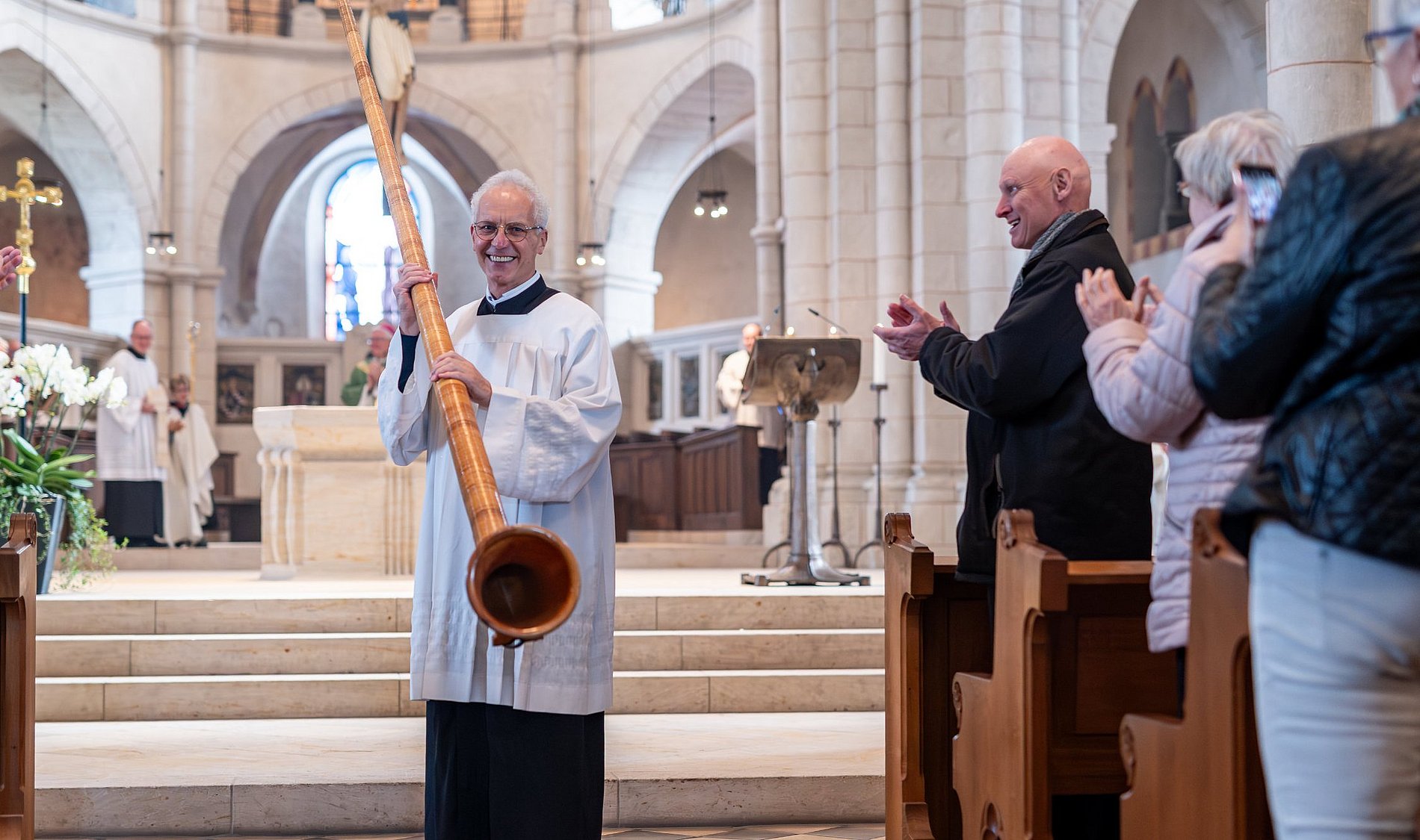 Bruder Elmar hält lächelnd sein Alphorn, die Gottesdienstbesucher applaudieren.