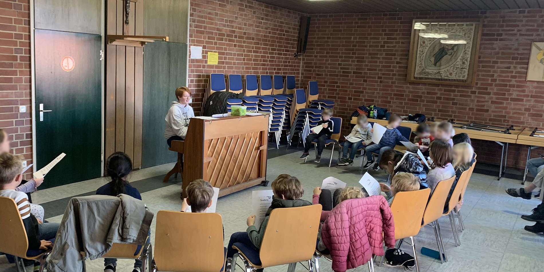 Kinder sitzen im Halbkreis und singen, begleitet von der Chorleiterin, die am Klavier spielt.