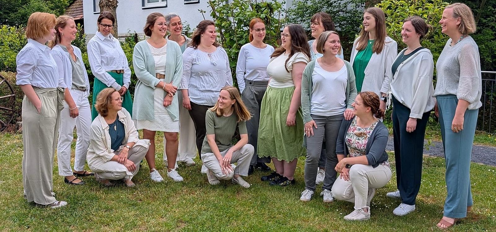 Eine Gruppe junger Frauen, die sich teilweise gegenseitig froh anblickend auf einer Wiese in einem Garten stehen.