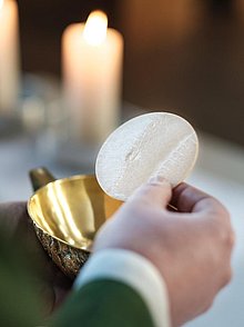 Der Priester hält eine Hostie über dem Kelch am Altar