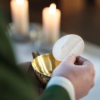 Der Priester hält eine Hostie über dem Kelch am Altar