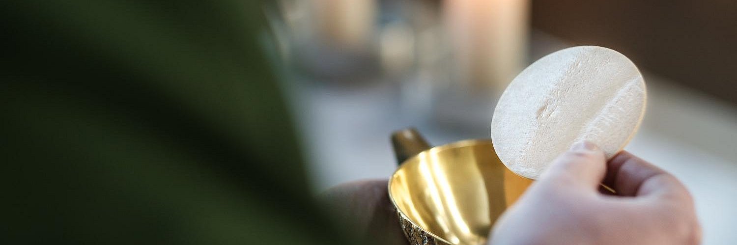 Der Priester hält eine Hostie über dem Kelch am Altar