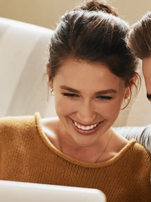 Junges Paar auf dem Sofa sitzend schauen in den Laptop und lachen