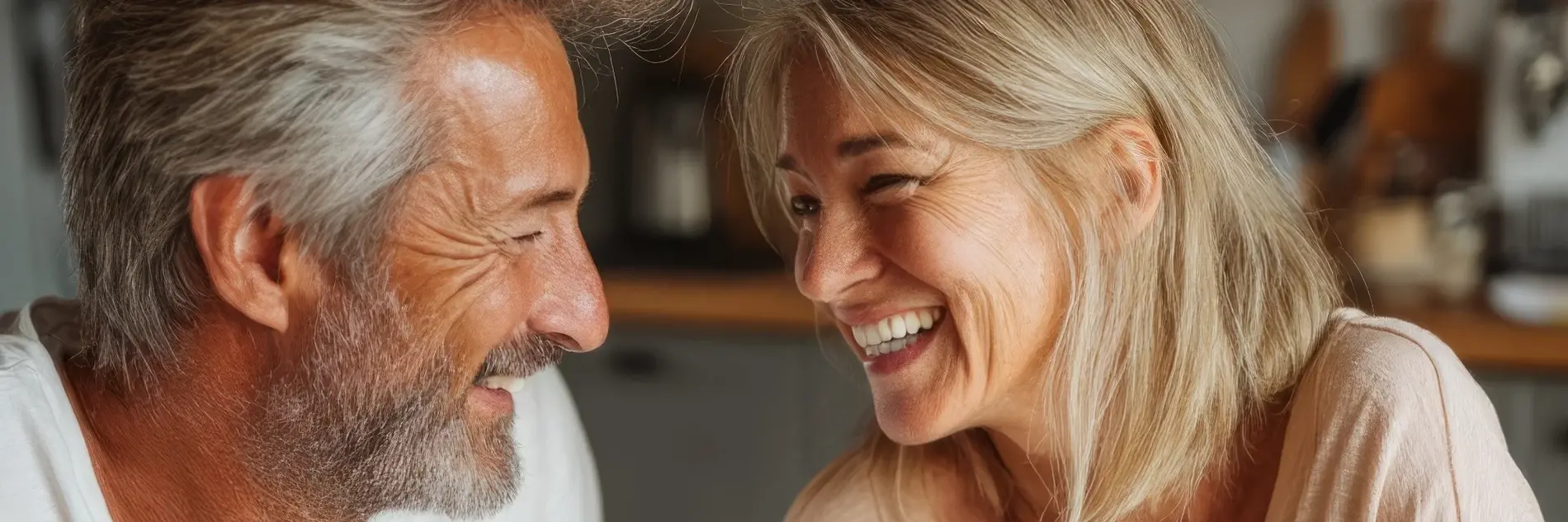 Paar mittleren Alters sitzt in der Küche und lacht zusammen