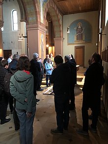 Menschen stehen in einer Kirche und hören einer Ordensschwester zu, die sie informiert.