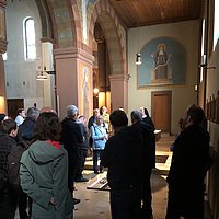 Menschen stehen in einer Kirche und hören einer Ordensschwester zu, die sie informiert.