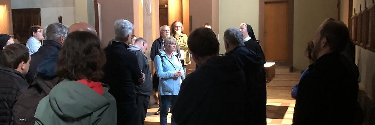 Menschen stehen in einer Kirche und hören einer Ordensschwester zu, die sie informiert.