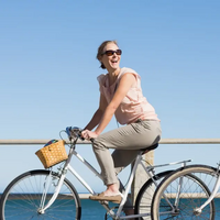 Ein Mann und eine Frau jeweils auf einem weißen Fahrrad fahrend und sich anlachend vor einem Geländer am Meer