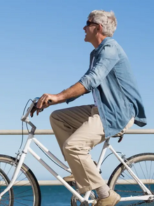 Ein Mann und eine Frau jeweils auf einem weißen Fahrrad fahrend und sich anlachend vor einem Geländer am Meer