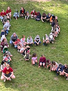 Kinder sitzen auf einer Wiese und bilden die Buchstaben SRE
