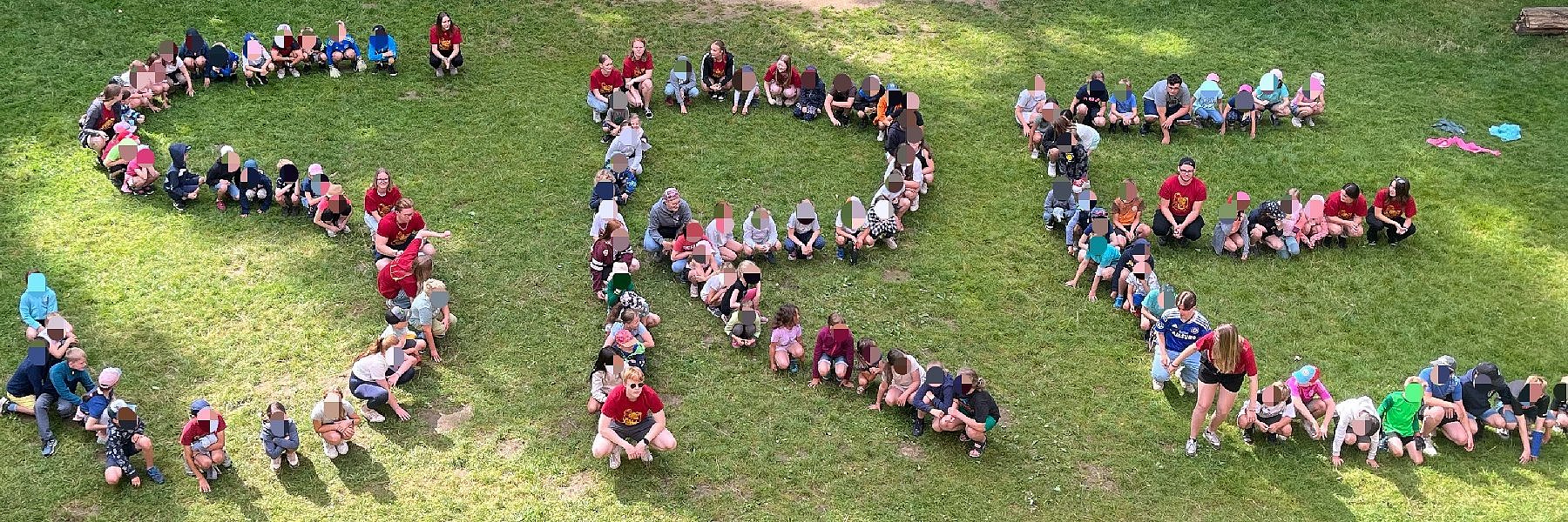 Kinder sitzen auf einer Wiese und bilden die Buchstaben SRE