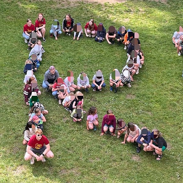 Kinder sitzen auf einer Wiese und bilden die Buchstaben SRE