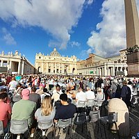Gläubige sitzen auf dem Petersplatz und warten auf die Papstaudienz