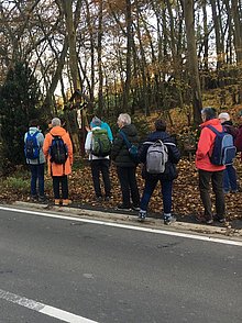 Die Pilgergruppe steht am Straßenrand vor einem Wegekreuz