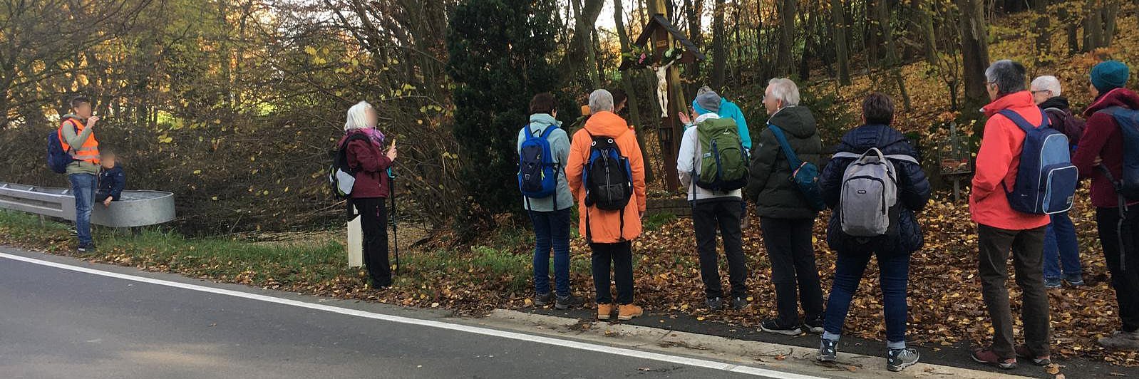 Die Pilgergruppe steht am Straßenrand vor einem Wegekreuz