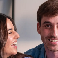 Junges Paar: der Mann lächelt in die Kamera, die Frau zu ihm.