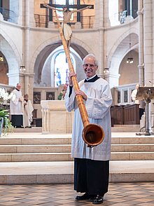 Bruder Elmar Mossbrugger hält sein Alphorn und lächelt, nachdem er im Dom für die Gottesdienstbesucher zum Abschied geblasen hat. Die Gottesdienstbesucher in den Reihen klatschen.