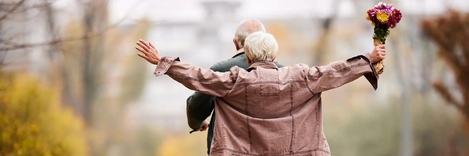 Ein älterer Mann hat seine Frau auf dem Gepäckträger und fährt mit dem Fahrrad - man sieht die beiden von hinten 