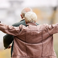 Ein älterer Mann hat seine Frau auf dem Gepäckträger und fährt mit dem Fahrrad - man sieht die beiden von hinten 